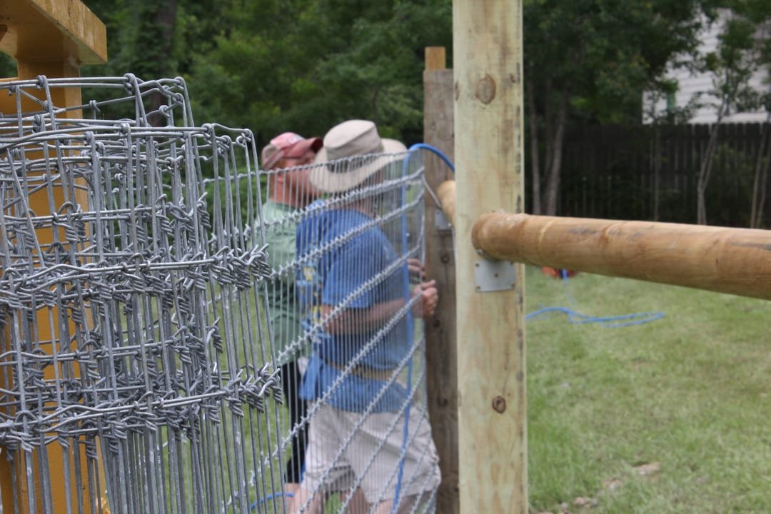 Crew stapling wire to the back of a wood rail fence