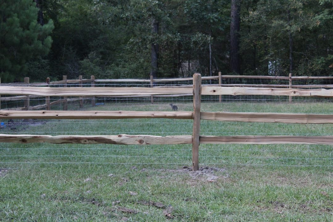 Wood rail fence with woven wire stretched behind it along a pasture