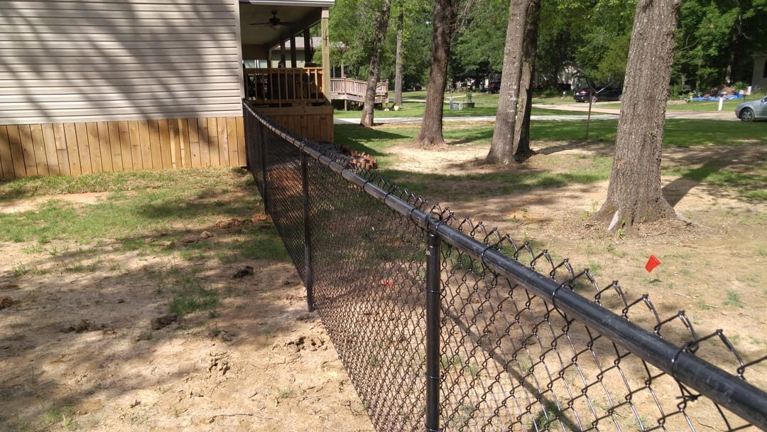 Black vinyl-coated chain link along a wooded yard