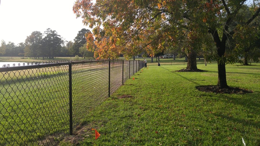 Black vinyl-coated chain link fence along a golf course edge
