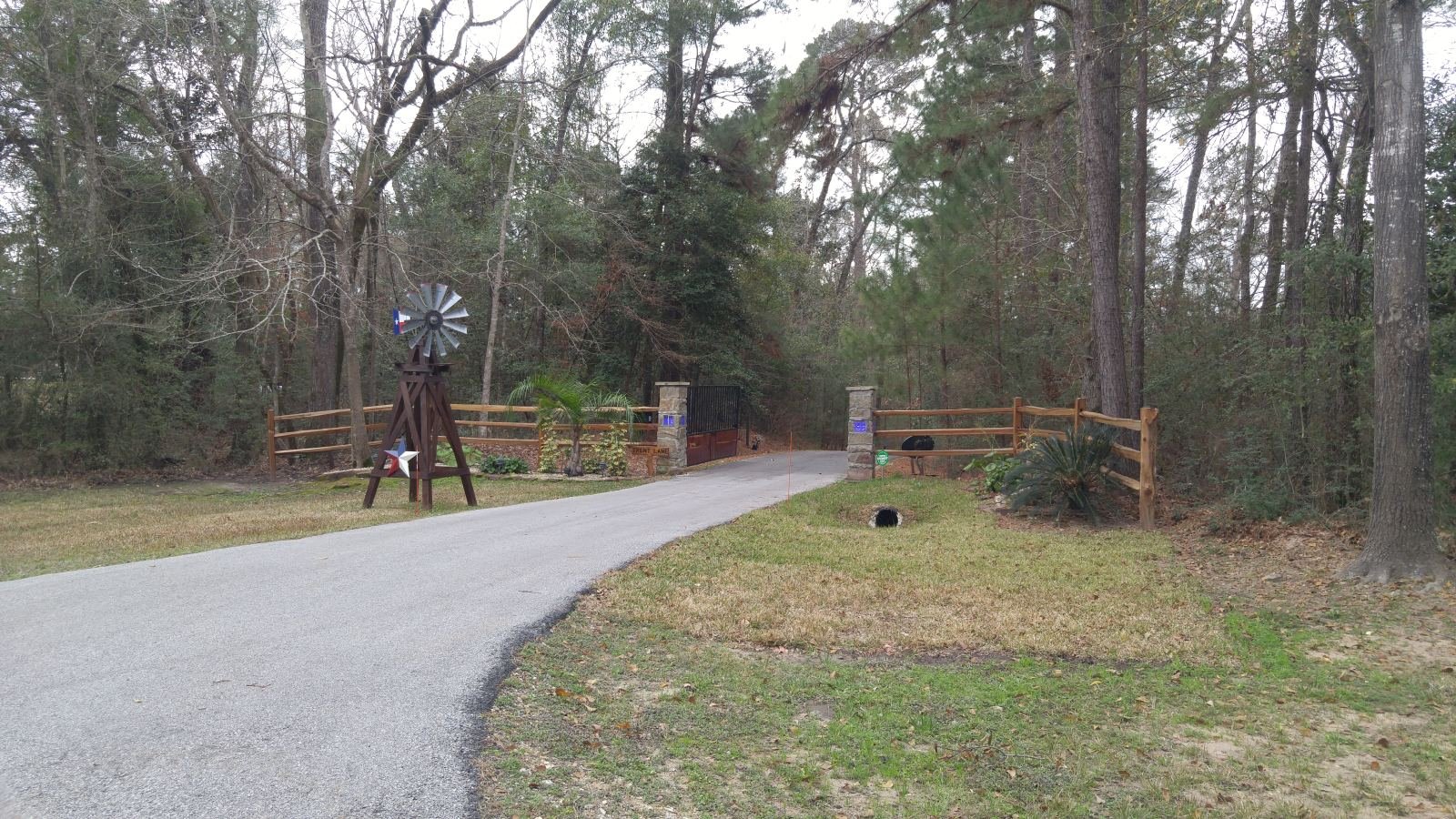 Ornamental black metal driveway gate with stone entrance columns and lamp